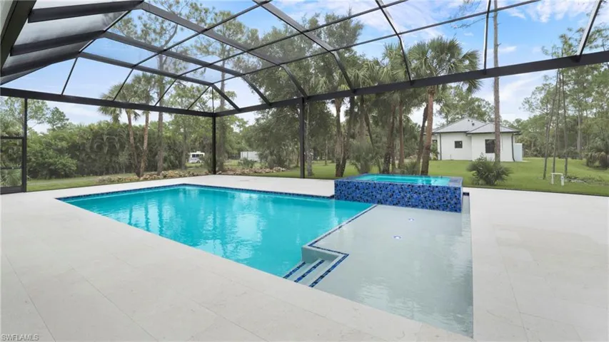 View of pool featuring glass enclosure, a lawn, a pool with connected hot tub, a patio, and a sunroom