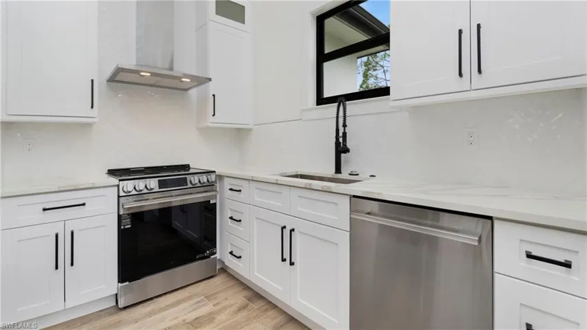 Kitchen featuring stainless steel appliances, wall chimney exhaust hood, decorative backsplash, white cabinetry, and light stone countertops