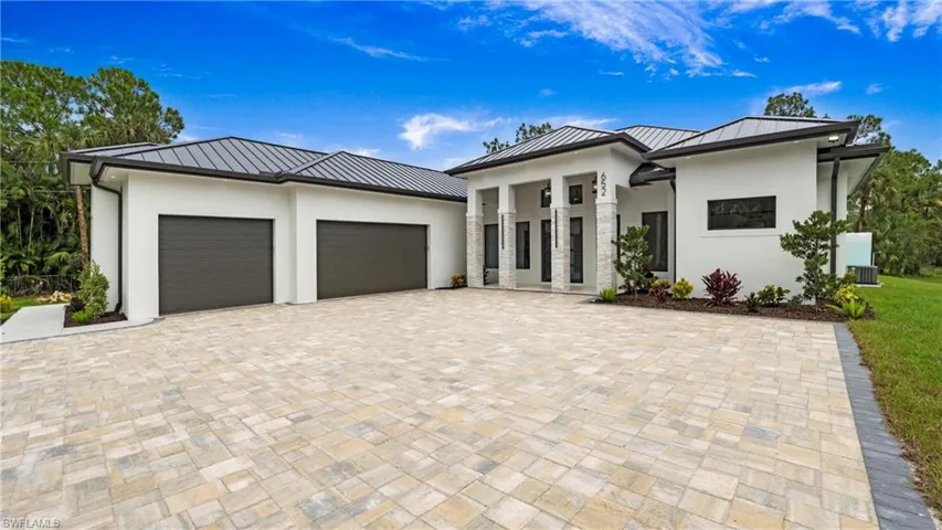 View of front of home with a standing seam roof, a metal roof, stucco siding, a garage, and decorative driveway