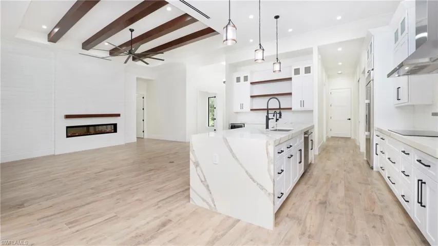 Kitchen with open shelves, glass insert cabinets, open floor plan, beamed ceiling, and wall chimney exhaust hood