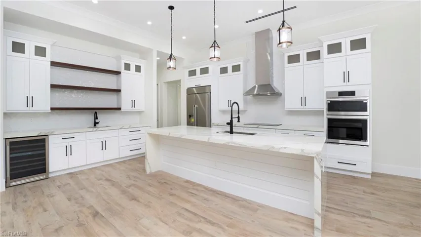 Kitchen featuring light stone countertops, wall chimney exhaust hood, open shelves, beverage cooler, and light wood finished floors