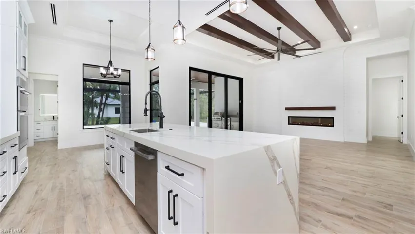 Kitchen featuring white cabinets, light wood finished floors, open floor plan, and beam ceiling