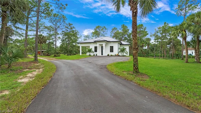 View of front facade featuring driveway, a front lawn, stucco siding, a metal roof, and a standing seam roof
