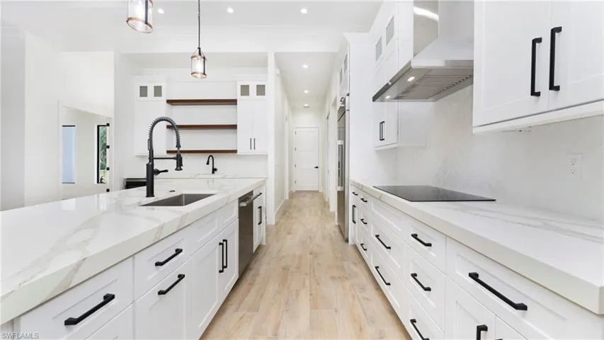 Kitchen featuring light stone counters, glass insert cabinets, open shelves, white cabinetry, and light wood-style floors