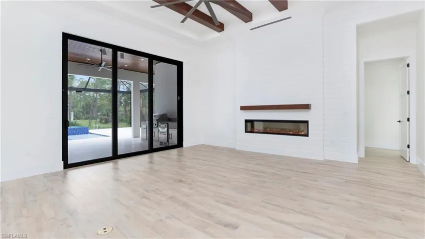 Unfurnished living room featuring light wood-style flooring, a glass covered fireplace, beamed ceiling, ceiling fan, and a towering ceiling