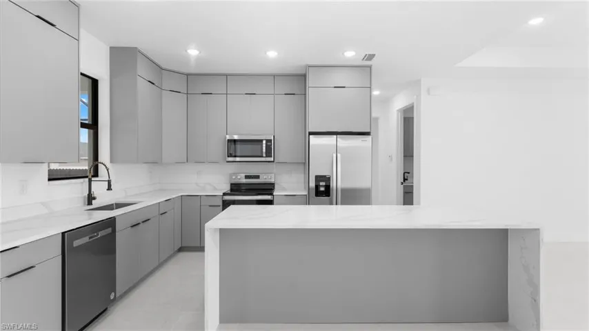 Kitchen with gray cabinetry, sink, appliances with stainless steel finishes, a kitchen island, and light stone counters