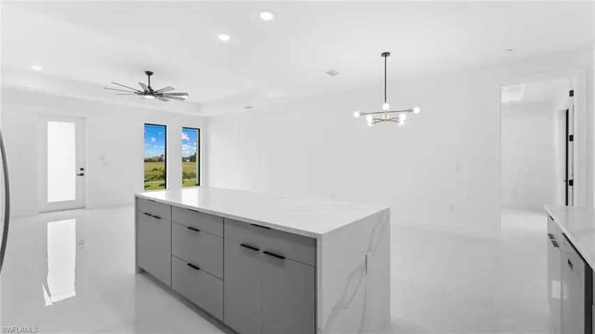 Kitchen featuring gray cabinetry, pendant lighting, ceiling fan with notable chandelier, a kitchen island, and light stone counters