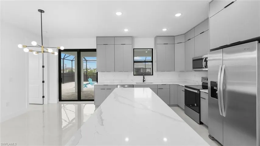 Kitchen with light stone countertops, stainless steel appliances, pendant lighting, a chandelier, and gray cabinets