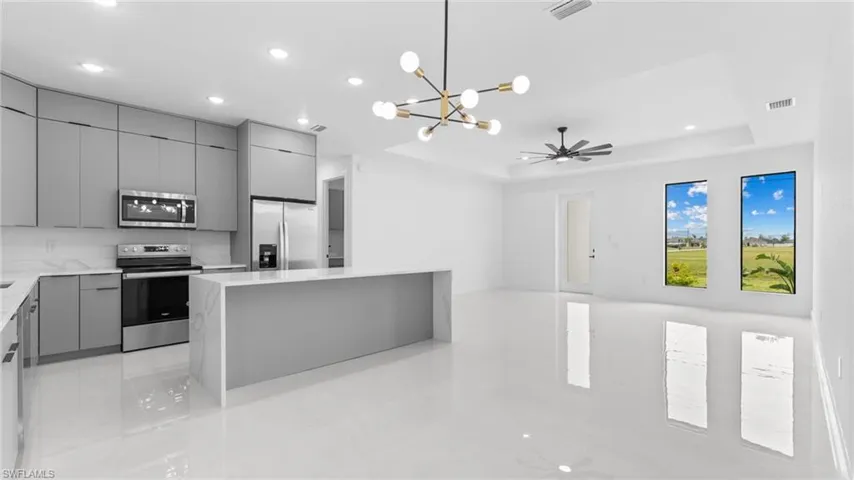 Kitchen featuring a center island, ceiling fan with notable chandelier, gray cabinets, a tray ceiling, and stainless steel appliances