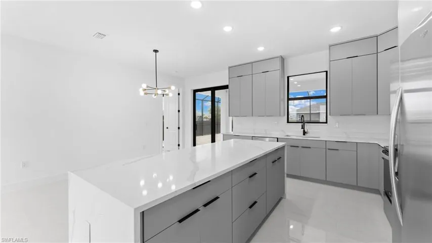Kitchen with gray cabinetry, a spacious island, sink, stainless steel fridge, and decorative light fixtures