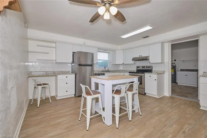 Kitchen with ceiling fan, light hardwood / wood-style flooring, white cabinetry, stainless steel appliances, and a breakfast bar area
