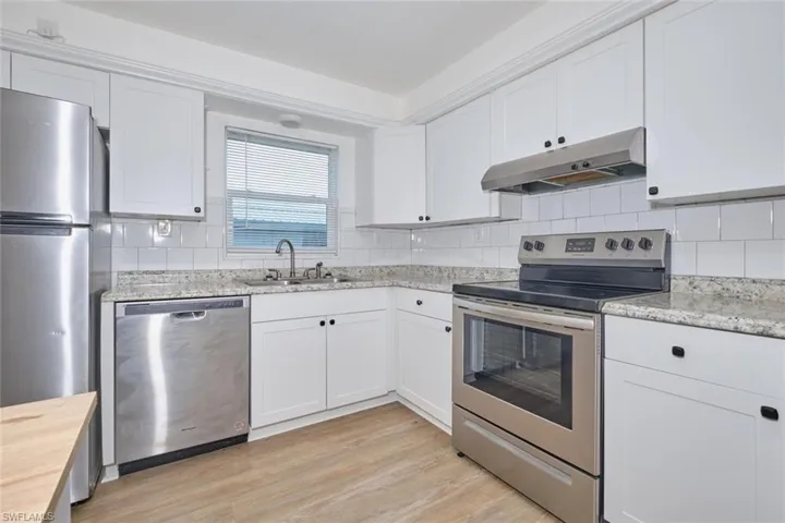 Kitchen with white cabinets, sink, tasteful backsplash, appliances with stainless steel finishes, and light hardwood / wood-style floors