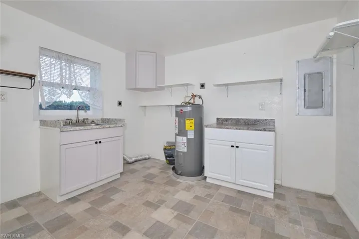 Kitchen featuring white cabinets, electric water heater, electric panel, and sink