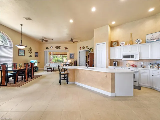 Kitchen featuring white appliances, tasteful backsplash, white cabinets, a large island with sink, and ceiling fan