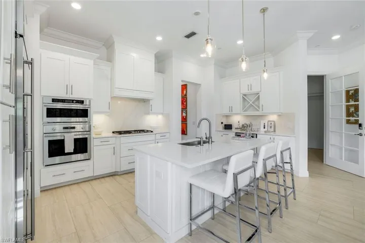 Kitchen featuring a breakfast bar, white cabinetry, tasteful backsplash, an island with sink, and ornamental molding