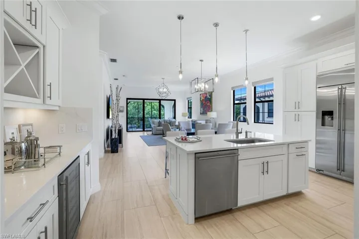 Kitchen with open floor plan, white cabinets, stainless steel appliances, a center island with sink, and decorative light fixtures