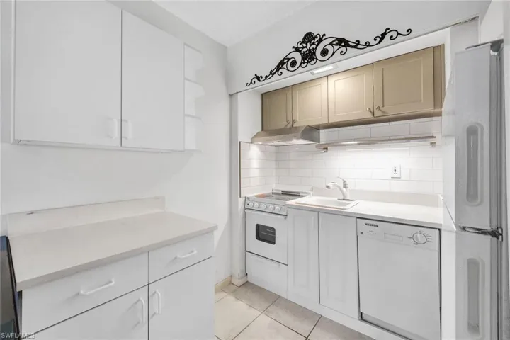 Kitchen featuring tasteful backsplash, white appliances, light tile floors, wall chimney exhaust hood, and sink
