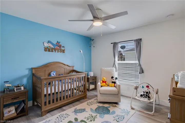 Bedroom featuring a crib, wood finished floors, and a ceiling fan