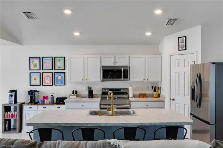 Kitchen featuring a center island with sink, stainless steel appliances, white cabinets, light countertops, and a breakfast bar area