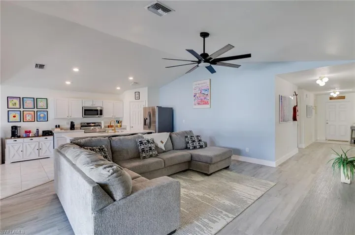 Living area with vaulted ceiling, a ceiling fan, and light wood-style flooring