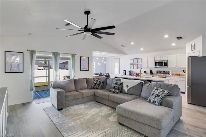Living room featuring ceiling fan, vaulted ceiling, light wood-style flooring, and suspended lighting