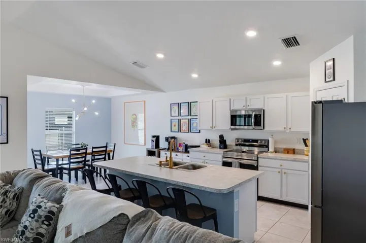Kitchen with a kitchen breakfast bar, stainless steel appliances, light countertops, white cabinetry, and vaulted ceiling