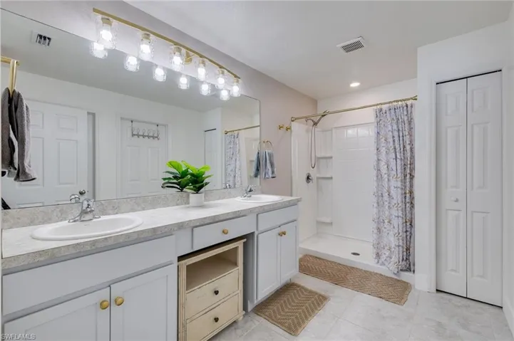 Bathroom with a closet, double vanity, a stall shower, and light tile patterned floors