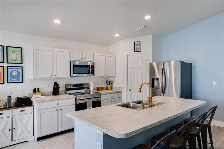 Kitchen with a breakfast bar, stainless steel appliances, an island with sink, light countertops, and recessed lighting