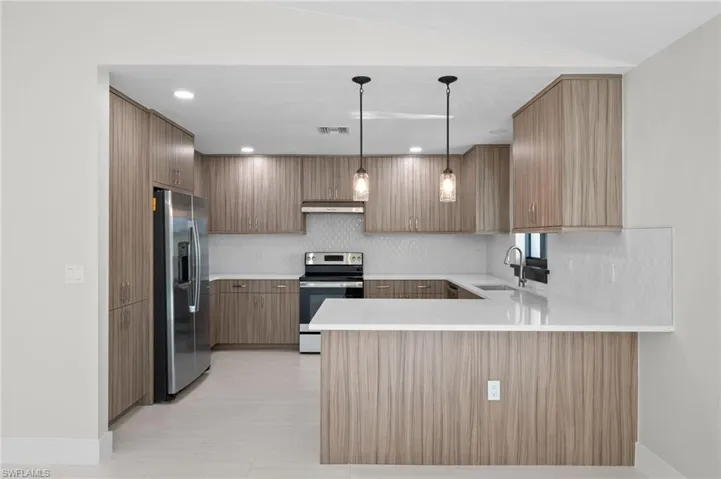 Kitchen featuring decorative light fixtures, stainless steel appliances, sink, kitchen peninsula, and backsplash