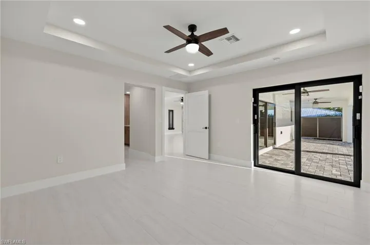 Empty room with ceiling fan, light tile patterned flooring, and a tray ceiling