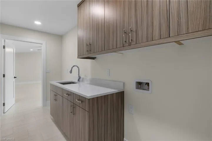 Clothes washing area featuring hookup for a washing machine, light tile patterned floors, cabinets, and sink