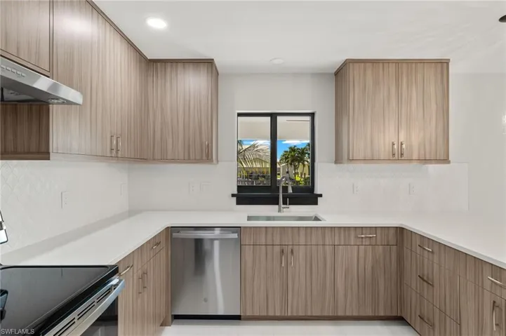 Kitchen featuring range, dishwashing machine, range hood, decorative backsplash, and sink