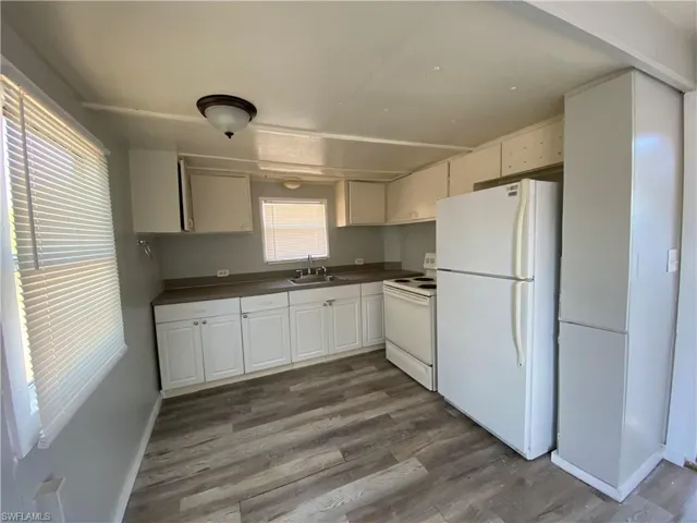 Kitchen with white appliances, dark countertops, dark wood-style flooring, and white cabinetry