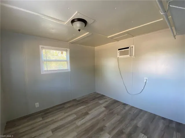Spare room with attic access, wood finished floors, and an AC wall unit