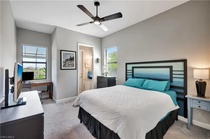 Bedroom with baseboards, light colored carpet, a ceiling fan, connected bathroom, and a desk