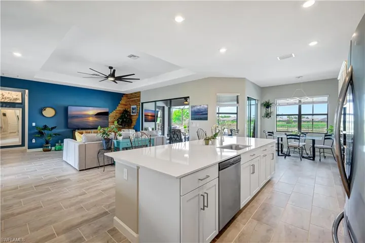 Kitchen with a sink, appliances with stainless steel finishes, light countertops, baseboards, and a center island with sink