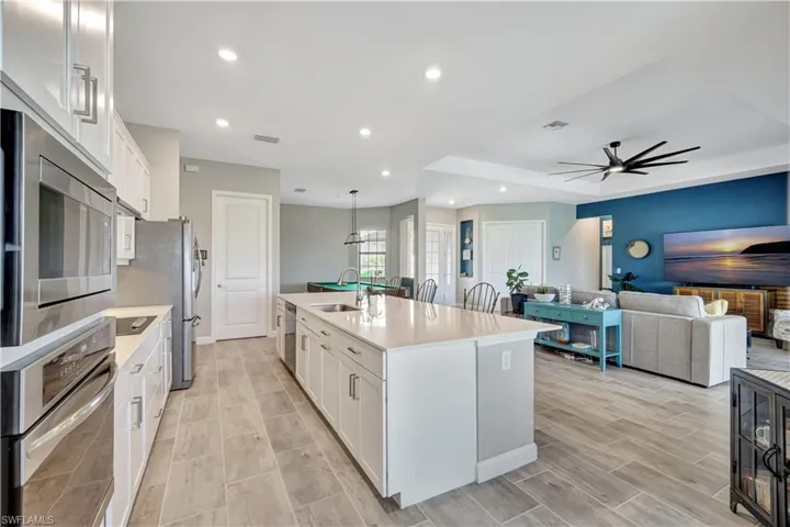 Kitchen with appliances with stainless steel finishes, a sink, light countertops, white cabinetry, and an island with sink