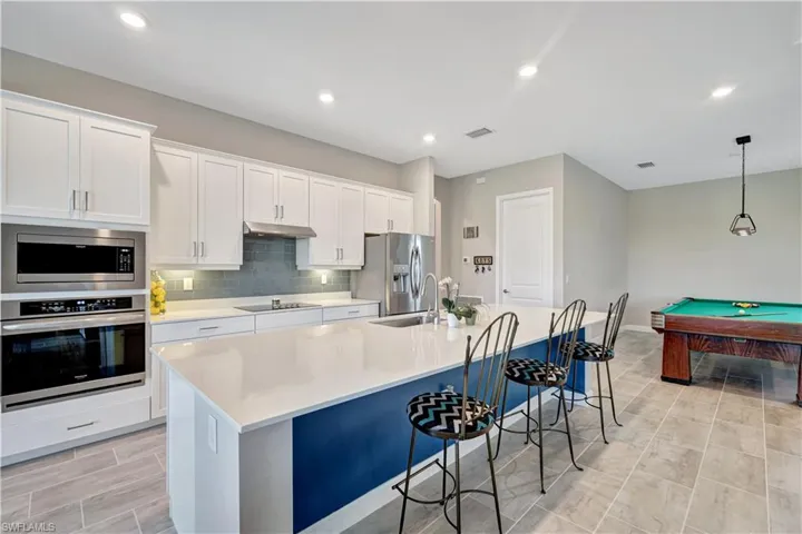 Kitchen featuring appliances with stainless steel finishes, under cabinet range hood, a large island with sink, a sink, and white cabinets
