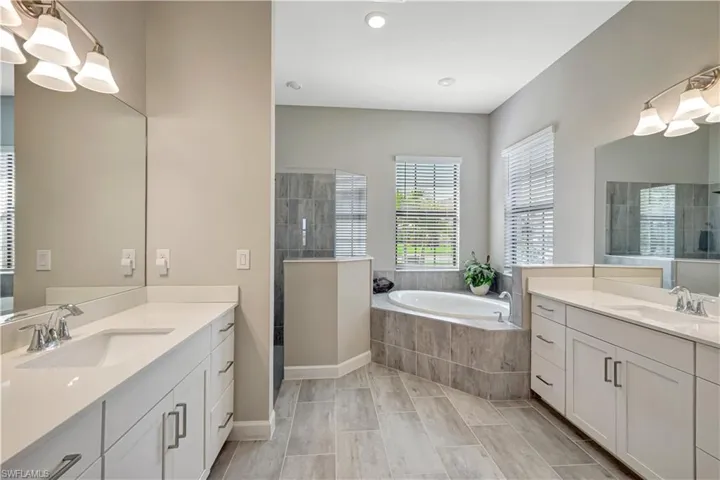 Full bathroom featuring two vanities, a garden tub, walk in shower, and recessed lighting