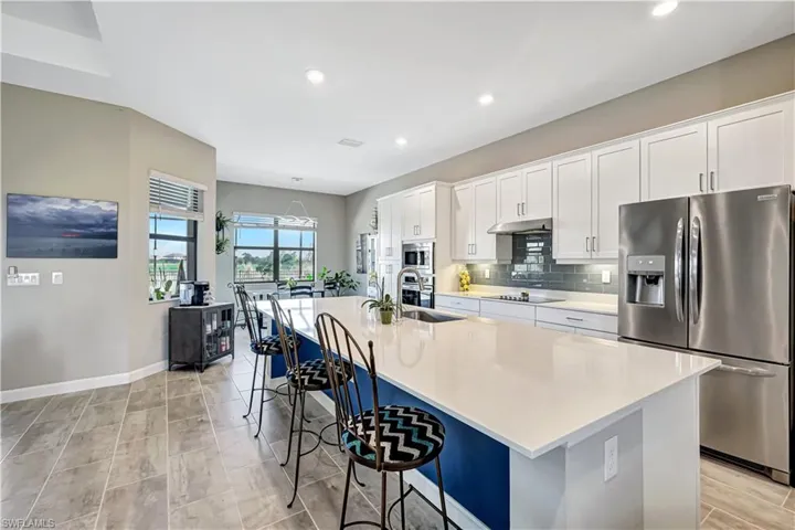 Kitchen with appliances with stainless steel finishes, a spacious island, a breakfast bar area, a sink, and white cabinetry