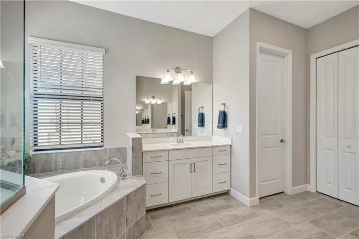 Bathroom featuring vanity, a closet, a garden tub, and tile patterned flooring