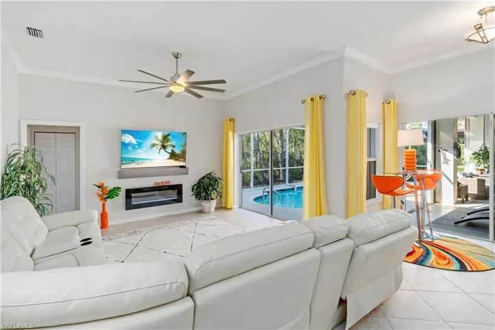 Living room with ornamental molding, tile patterned floors, healthy amount of natural light, a ceiling fan, and a glass covered fireplace