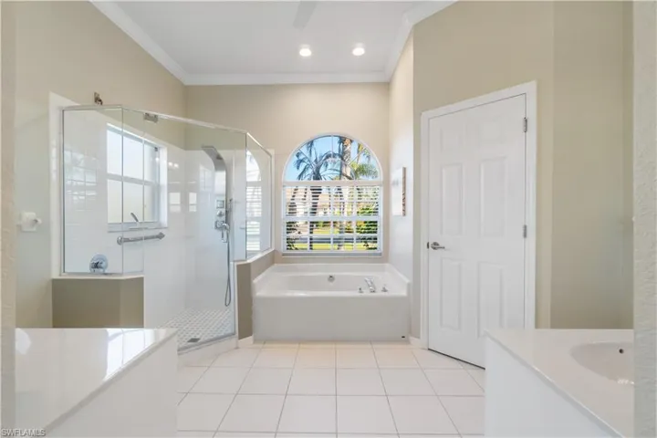 Full bathroom featuring light tile patterned floors, a garden tub, a stall shower, vanity, and crown molding