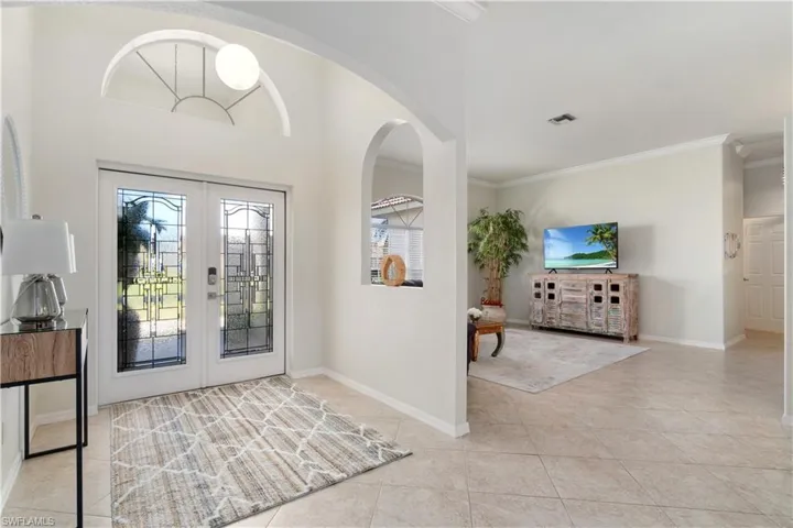 Foyer with french doors, crown molding, arched walkways, and light tile patterned floors