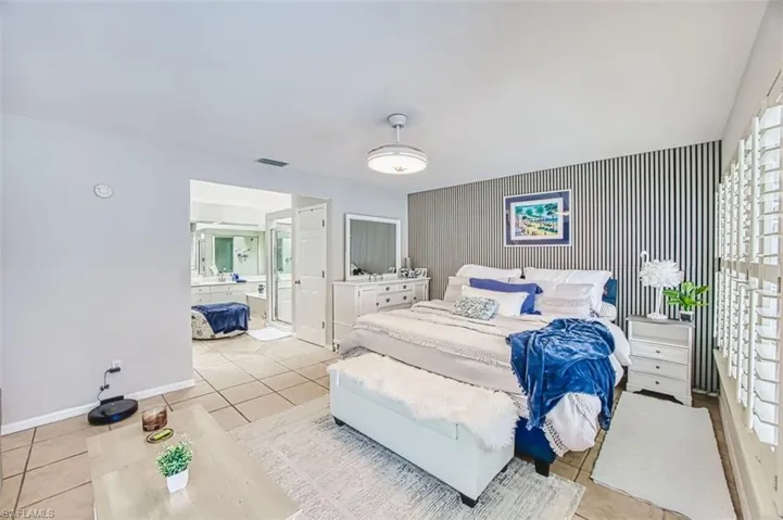 Bedroom featuring an accent wall, light tile patterned flooring, wallpapered walls, and multiple windows