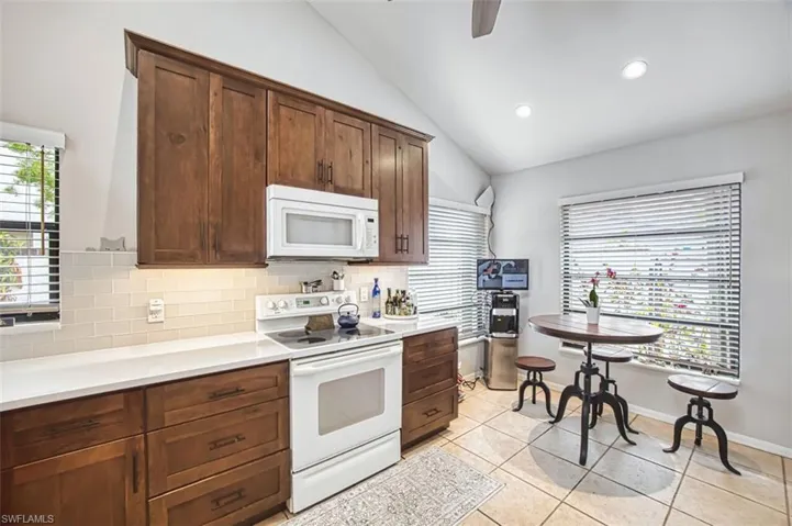 Kitchen with white appliances, a ceiling fan, light tile patterned flooring, lofted ceiling, and decorative backsplash
