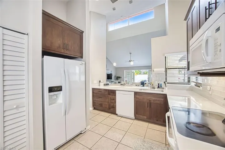Kitchen featuring a ceiling fan, white appliances, dark wood finish cabinetry, a high ceiling, and decorative backsplash