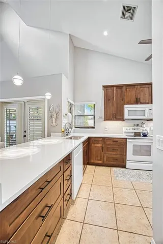 Kitchen featuring vaulted ceiling, hanging light fixtures, white appliances, light tile patterned floors, and ceiling fan