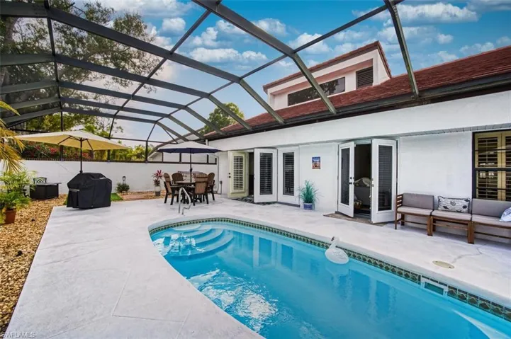 View of pool featuring a sunroom, a grill, glass enclosure, outdoor dining area, and patio surround