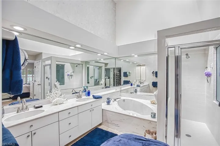 Ensuite bathroom with a shower stall, double vanity, a high ceiling, a garden tub, and recessed lighting